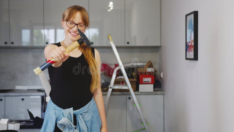 Caucasian young woman with long blond hair showing a hammer to the camera, medium shot kitchen repair concept. High quality photo. Caucasian young woman with long blond hair showing a hammer to the camera, medium shot kitchen repair concept. High quality photo