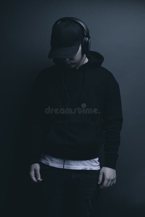 Young cool rapper with black hoodie and cap looking down and listening music. Young cool rapper with black hoodie and cap looking down and listening music.