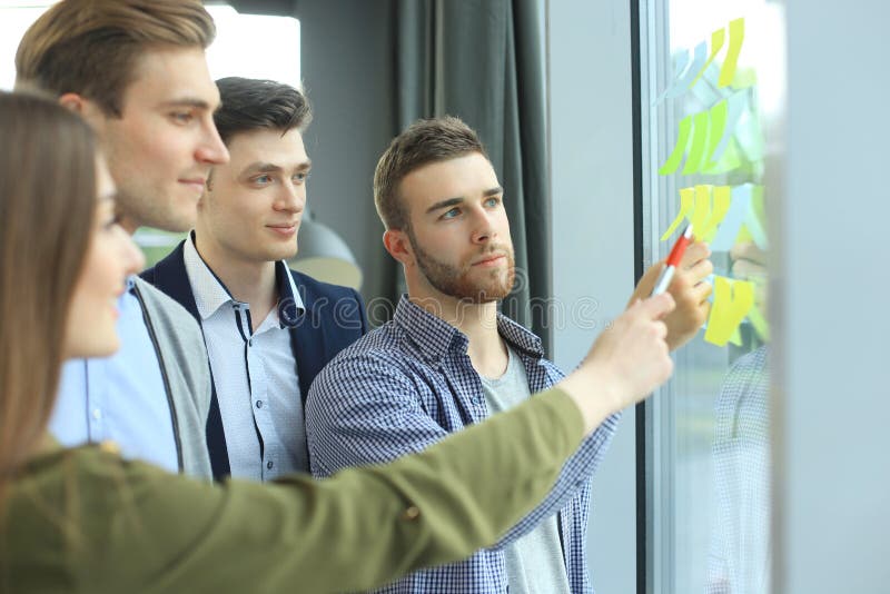 Jonge creatieve startmensen op vergadering die op modern kantoor plannen en projecten met poststickers op glas maken stock afbeelding Jonge creatieve startmensen op vergadering die op modern kantoor plannen en projecten met poststickers op glas maken stock afbeelding