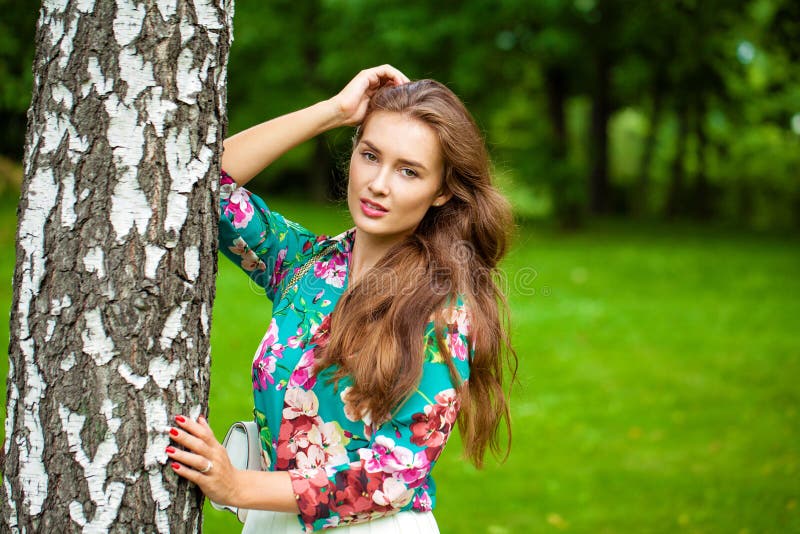 Young happy brunette woman in flowers blouse in the summer park. Young happy brunette woman in flowers blouse in the summer park