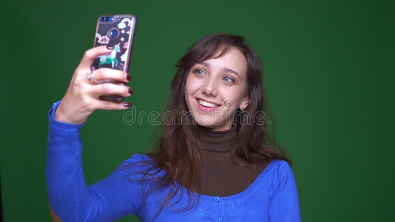 Jonge donkerbruine vrouwelijke student die selfie-foto's smilingly op smartphone op groene achtergrond schieten