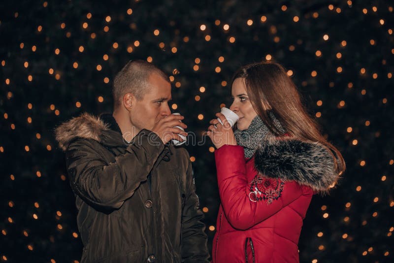 Young cheerful couple outdoors on a winter eve, with hot drinks, looking at each other, so tender, romantic, tempting, sensual. True love and feelings. Young cheerful couple outdoors on a winter eve, with hot drinks, looking at each other, so tender, romantic, tempting, sensual. True love and feelings