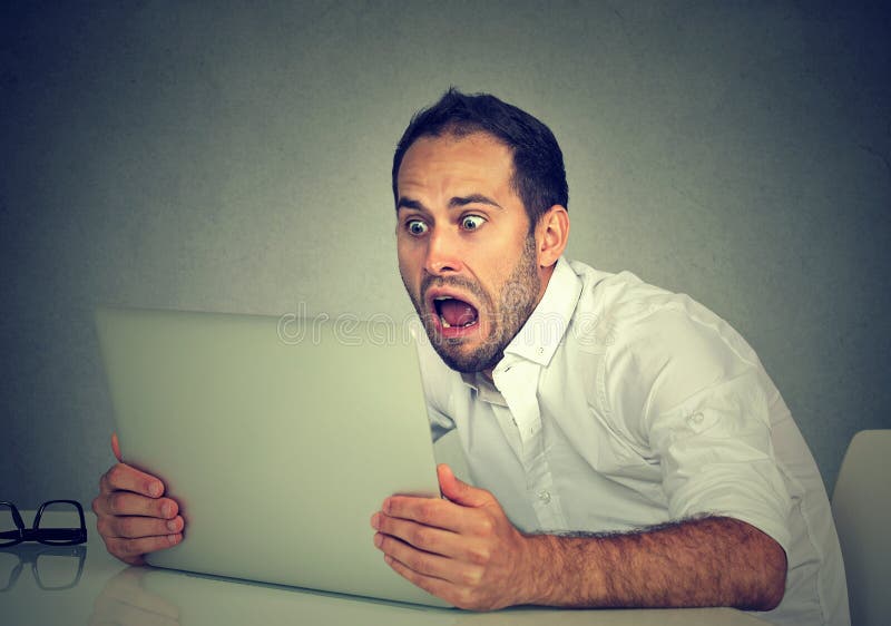 Jonge geschokte mens met laptop computerzitting bij lijst royalty-vrije stock foto Jonge geschokte mens met laptop computerzitting bij lijst royalty-vrije stock foto