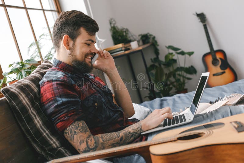 Jonge gitarist hipster thuis met gitaar in slaapkamertelefoongesprek royalty-vrije stock afbeeldingen Jonge gitarist hipster thuis met gitaar in slaapkamertelefoongesprek royalty-vrije stock afbeeldingen