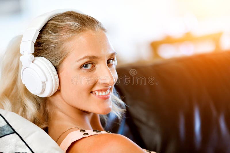 Jonge glimlachende vrouw die met hoofdtelefoons op de bank ontspannen die aan muziek luisteren die online een smartphone gebruike royalty-vrije stock foto Jonge glimlachende vrouw die met hoofdtelefoons op de bank ontspannen die aan muziek luisteren die online een smartphone gebruike royalty-vrije stock foto