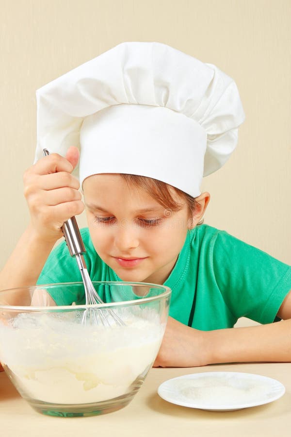 Jonge grappige jongen in de schuifelgangdeeg van de chef-kokshoed voor bakselcake royalty-vrije stock foto Jonge grappige jongen in de schuifelgangdeeg van de chef-kokshoed voor bakselcake royalty-vrije stock foto