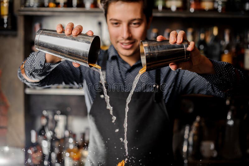 Jonge het glimlachen barman gietende drank met plakken van vers oranje fruit stock fotografie Jonge het glimlachen barman gietende drank met plakken van vers oranje fruit stock fotografie