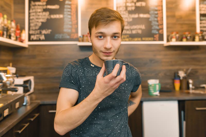 Jonge het glimlachen mannelijke barista drinkt koffie in koffiewinkel, geniet de mens van verse geurige koffie royalty-vrije stock afbeelding Jonge het glimlachen mannelijke barista drinkt koffie in koffiewinkel, geniet de mens van verse geurige koffie royalty-vrije stock afbeelding