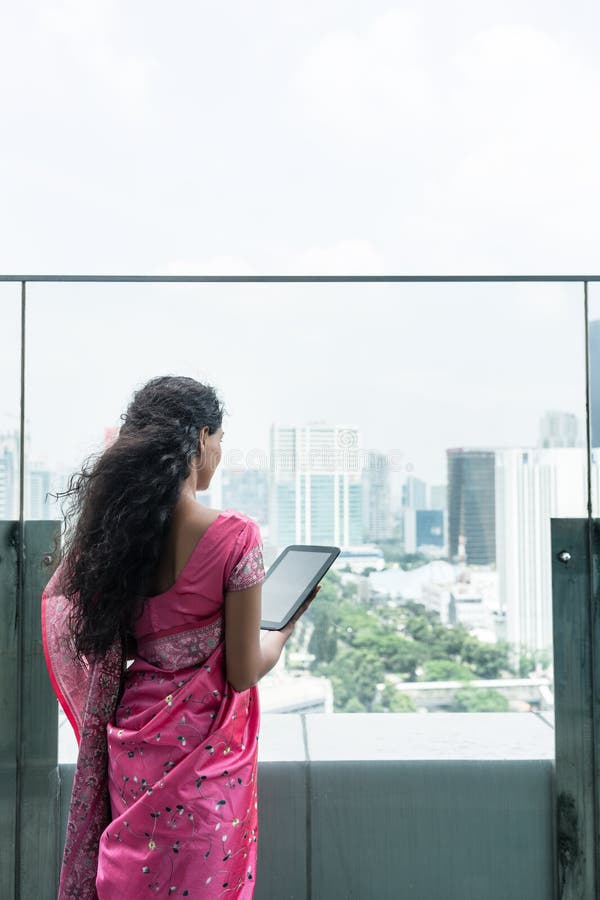 Jonge Indische vrouw die een tabletpc op een terras in een winderige dag met behulp van stock afbeelding Jonge Indische vrouw die een tabletpc op een terras in een winderige dag met behulp van stock afbeelding