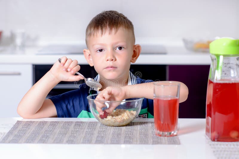 Young boy eating his lunch table kitchen grinning at camera as he puts his hand bowl to grab some food. Young boy eating his lunch table kitchen grinning at camera as he puts his hand bowl to grab some food