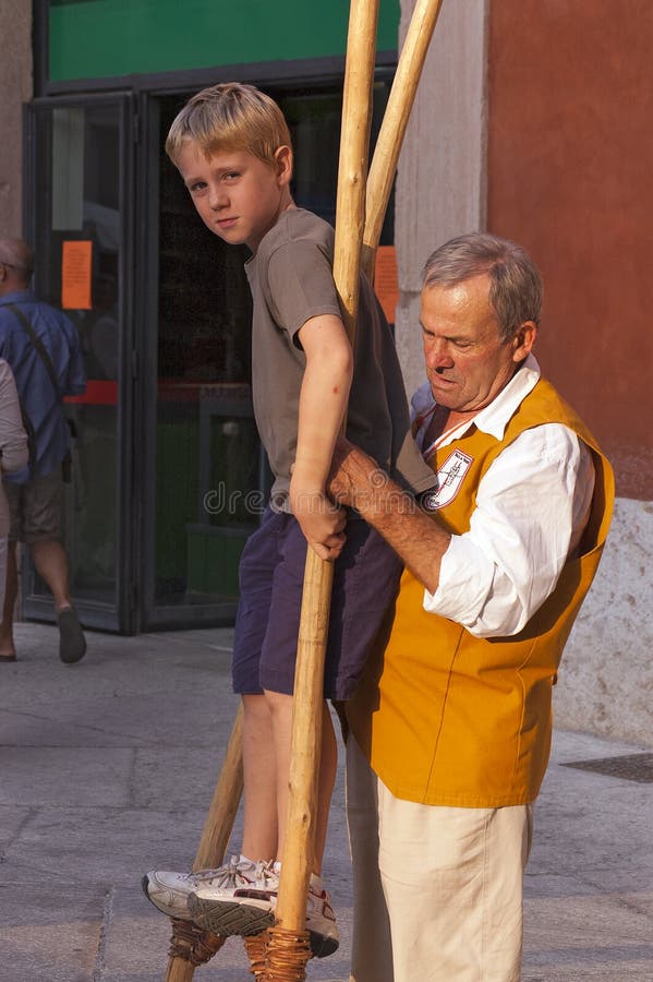 VERONA, ITALY - SEPTEMBER 24, 2011: Tocati, International festival of street games. An instructor of the Schieti village (Urbino Italy) teaches a young boy to stay balanced on wooden stilts. VERONA, ITALY - SEPTEMBER 24, 2011: Tocati, International festival of street games. An instructor of the Schieti village (Urbino Italy) teaches a young boy to stay balanced on wooden stilts