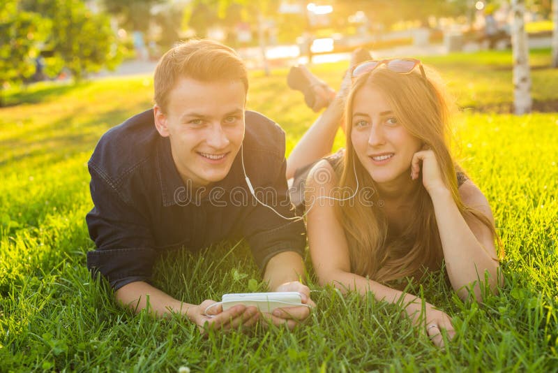 Jonge Kaukasische mooie paar of studenten die samen op het gras liggen die, aan muziek luisteren Liefde royalty-vrije stock afbeelding Jonge Kaukasische mooie paar of studenten die samen op het gras liggen die, aan muziek luisteren Liefde royalty-vrije stock afbeelding