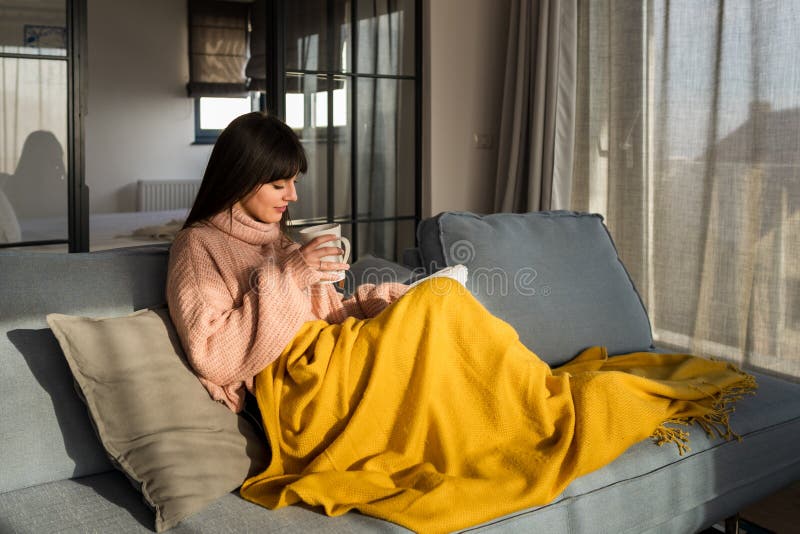 Jonge kaukasische vrouw die rustig zit met een gele deken op een grijze bank