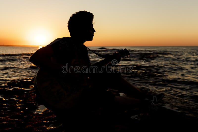 Jonge kerel die een gitaar spelen bij zonsondergang stock fotografie Jonge kerel die een gitaar spelen bij zonsondergang stock fotografie