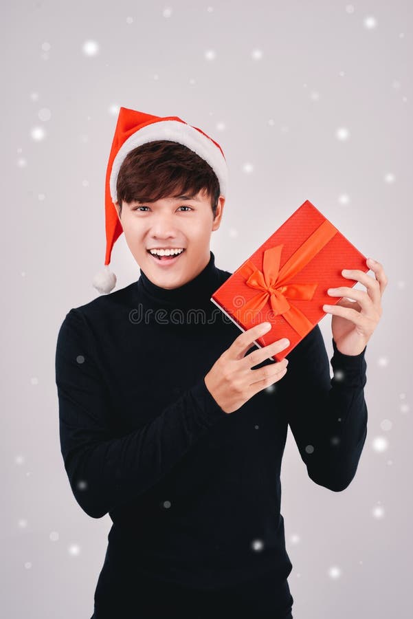 Jonge knappe Aziatische mens die met geïsoleerde santahoed een gift houden, royalty-vrije stock foto's Jonge knappe Aziatische mens die met geïsoleerde santahoed een gift houden, royalty-vrije stock foto's