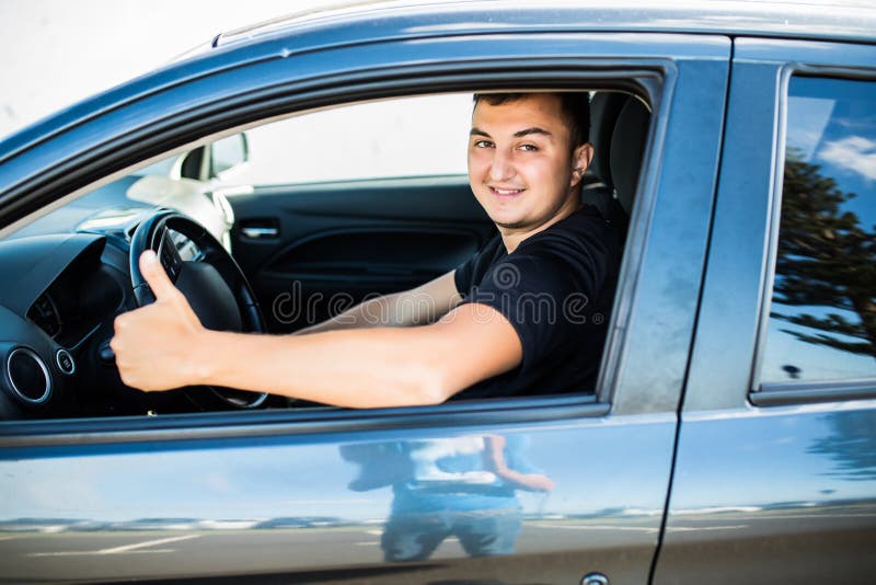 Jonge knappe mens die en duimen in zijn auto glimlachen tonen royalty-vrije stock afbeeldingen Jonge knappe mens die en duimen in zijn auto glimlachen tonen royalty-vrije stock afbeeldingen