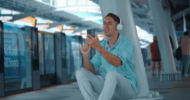 Jonge man met een oortelefoon wacht op de metro op het station en praat telefonisch. actieve man leidt online