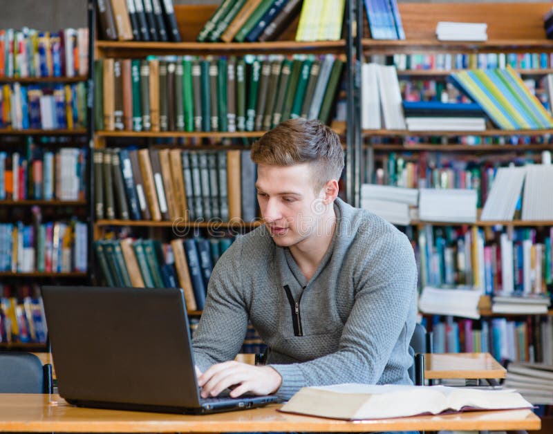 Jonge mannelijke student die laptop in de universitaire bibliotheek met behulp van royalty-vrije stock foto Jonge mannelijke student die laptop in de universitaire bibliotheek met behulp van royalty-vrije stock foto