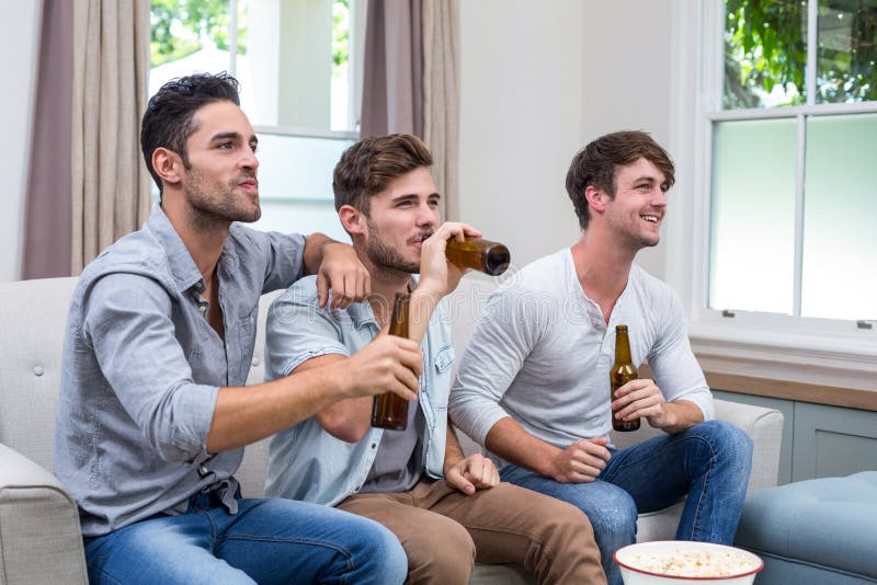 Jonge mannelijke vrienden die bier drinken terwijl het letten van op TV stock afbeeldingen Jonge mannelijke vrienden die bier drinken terwijl het letten van op TV stock afbeeldingen