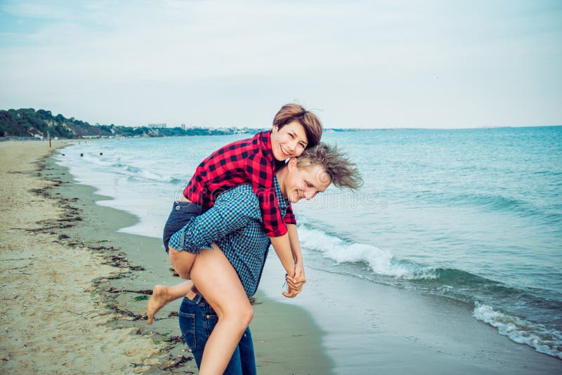 Jonge mannen die op de rug rit geven aan vrouwen op strand Jong paar die pret samen met blauwe oceaanachtergrond hebben Concept m stock afbeelding Jonge mannen die op de rug rit geven aan vrouwen op strand Jong paar die pret samen met blauwe oceaanachtergrond hebben Concept m stock afbeelding