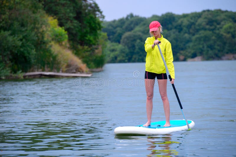 Jonge meisje-surfer die op de stand-up peddelraad berijden in de duidelijke wateren van de achtergrond van groene bomen stock foto's Jonge meisje-surfer die op de stand-up peddelraad berijden in de duidelijke wateren van de achtergrond van groene bomen stock foto's