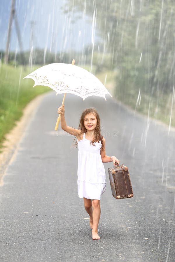 Young girl walks with suitcase and umbrella in the rain on empty road. Young girl walks with suitcase and umbrella in the rain on empty road