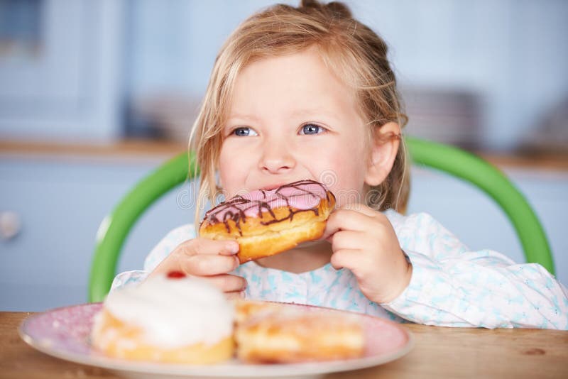 Jonge Meisjeszitting bij Lijst die Bevroren Doughnut eten royalty-vrije stock foto Jonge Meisjeszitting bij Lijst die Bevroren Doughnut eten royalty-vrije stock foto