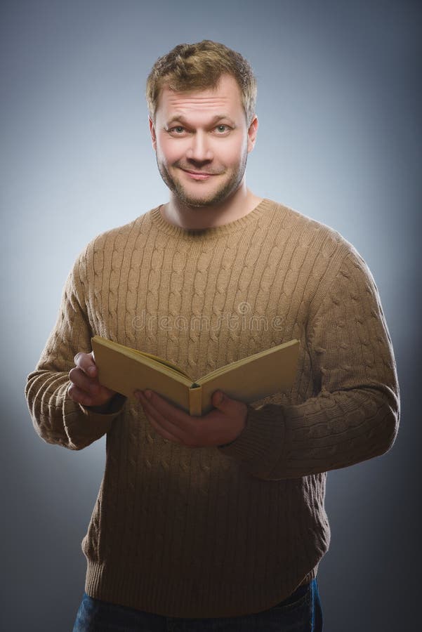 Jonge mens die een boek lezen en op grijze achtergrond glimlachen stock fotografie Jonge mens die een boek lezen en op grijze achtergrond glimlachen stock fotografie