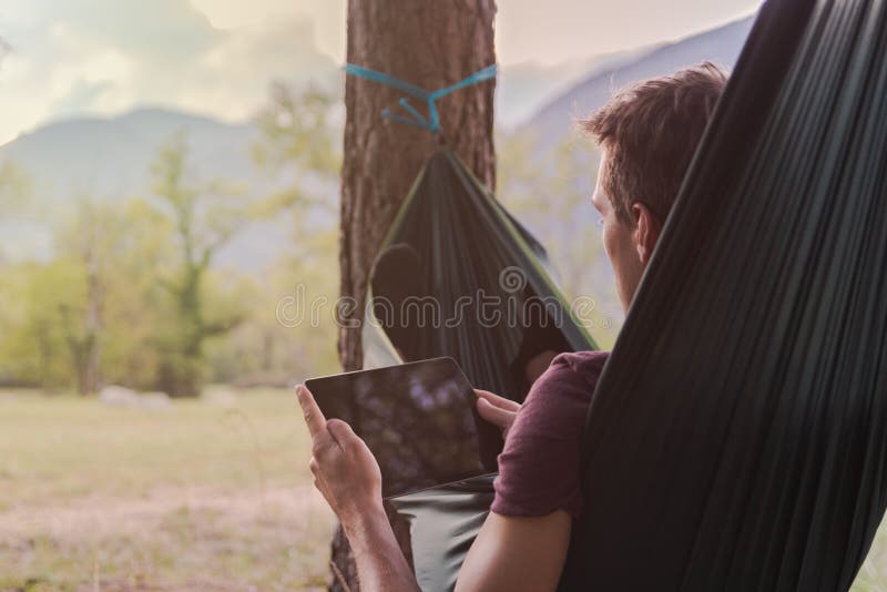Jonge mens die een tablet op een hangmat gebruiken stock fotografie Jonge mens die een tablet op een hangmat gebruiken stock fotografie