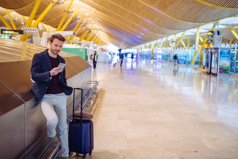 Jonge mens die en mobiele telefoon wachten met behulp van bij de luchthaven stock foto's Jonge mens die en mobiele telefoon wachten met behulp van bij de luchthaven stock foto's