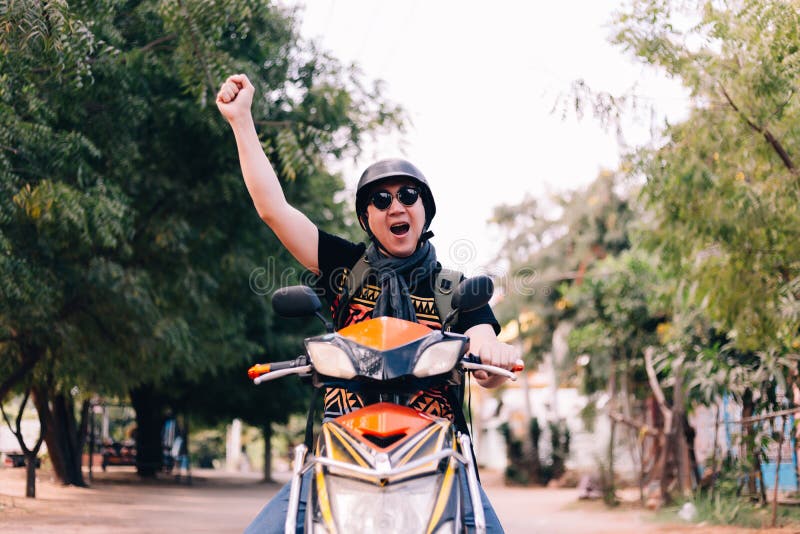 Jonge mens die in zonnebril en helm berijdende motorfiets handen opheffen omhoog als winnaar en succes royalty-vrije stock afbeelding Jonge mens die in zonnebril en helm berijdende motorfiets handen opheffen omhoog als winnaar en succes royalty-vrije stock afbeelding