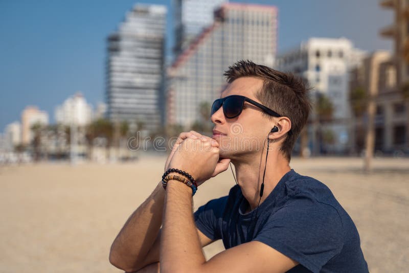 Jonge mens op de strand het luisteren muziek met hoofdtelefoons stadshorizon als achtergrond stock foto's Jonge mens op de strand het luisteren muziek met hoofdtelefoons stadshorizon als achtergrond stock foto's