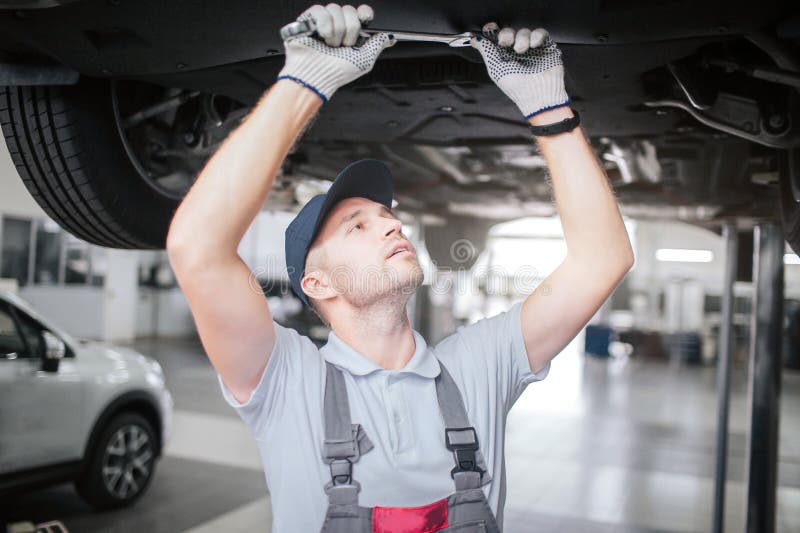 Jonge mens in proces om onderaan auto te werken Hij kijkt omhoog aan recht en greep grote moersleutel met beide handen Hij is royalty-vrije stock fotografie Jonge mens in proces om onderaan auto te werken Hij kijkt omhoog aan recht en greep grote moersleutel met beide handen Hij is royalty-vrije stock fotografie