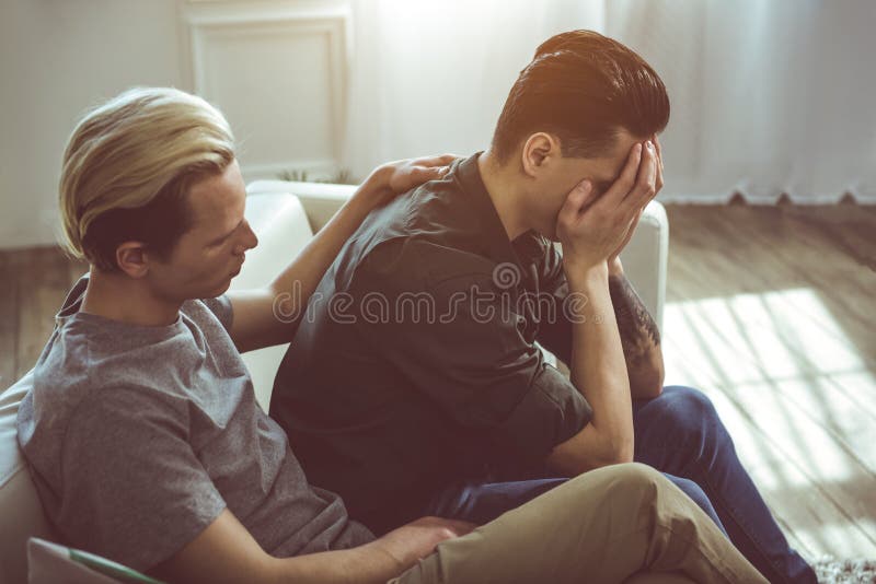 Jonge mensen troostende vriend terwijl hij die gezicht behandelen met wapens stock fotografie Jonge mensen troostende vriend terwijl hij die gezicht behandelen met wapens stock fotografie