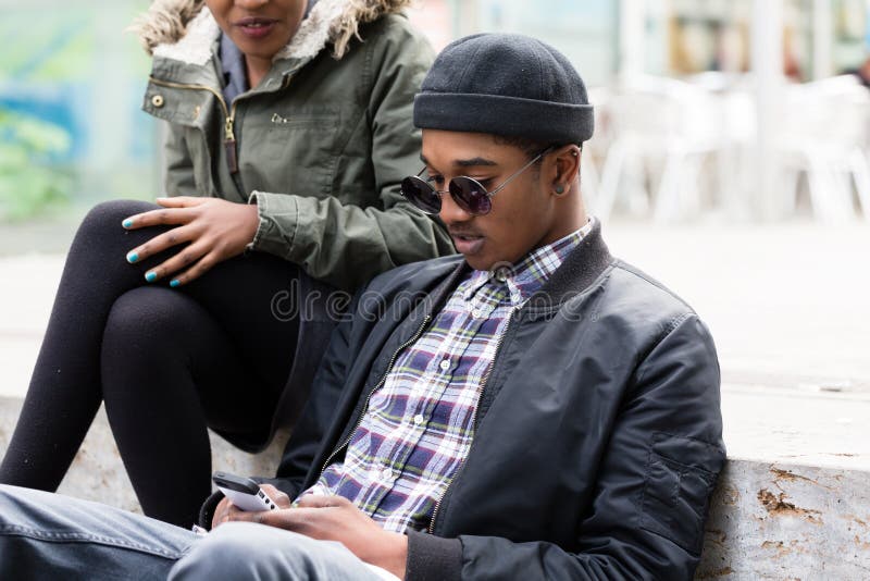 Jonge mensenzitting met zijn meisje mobiel gebruiken stock afbeelding Jonge mensenzitting met zijn meisje mobiel gebruiken stock afbeelding