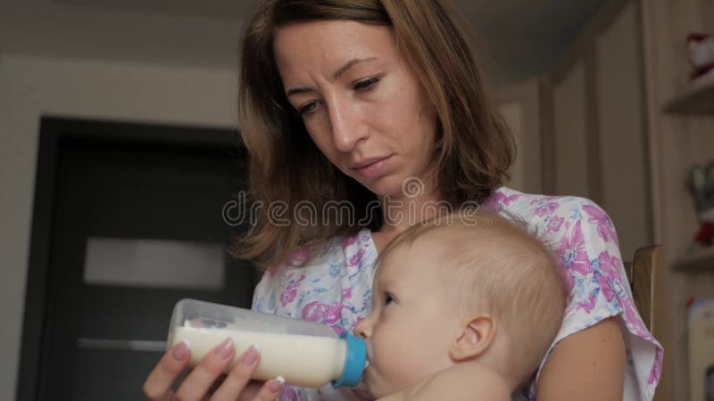 Jonge moeder die haar babyzoon met een fles melk thuis voeden