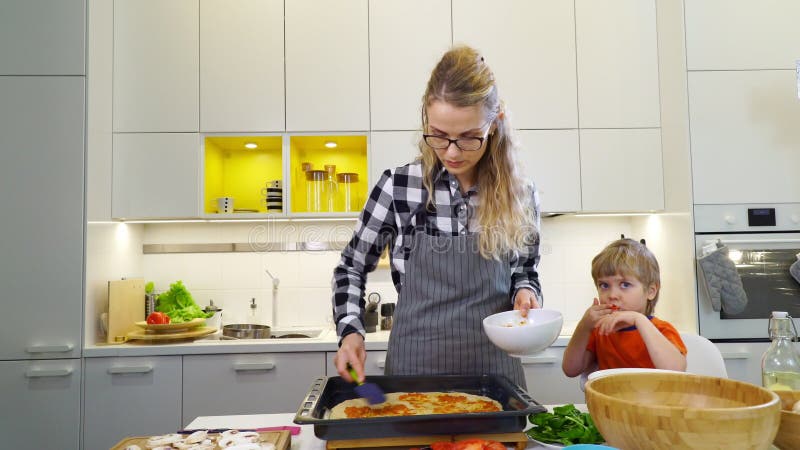 Jonge moeder die tomatensaus op de pizza zetten