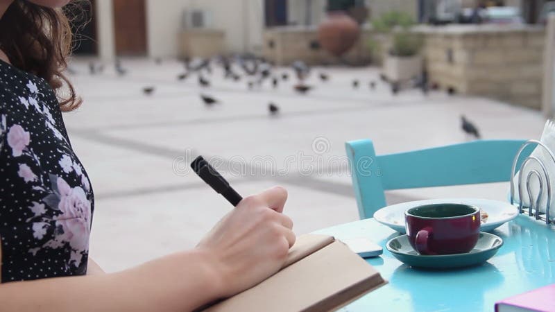Jonge mooie dame die in notitieboekje tijdens middagpauze in koffie schrijven, die nota's maken