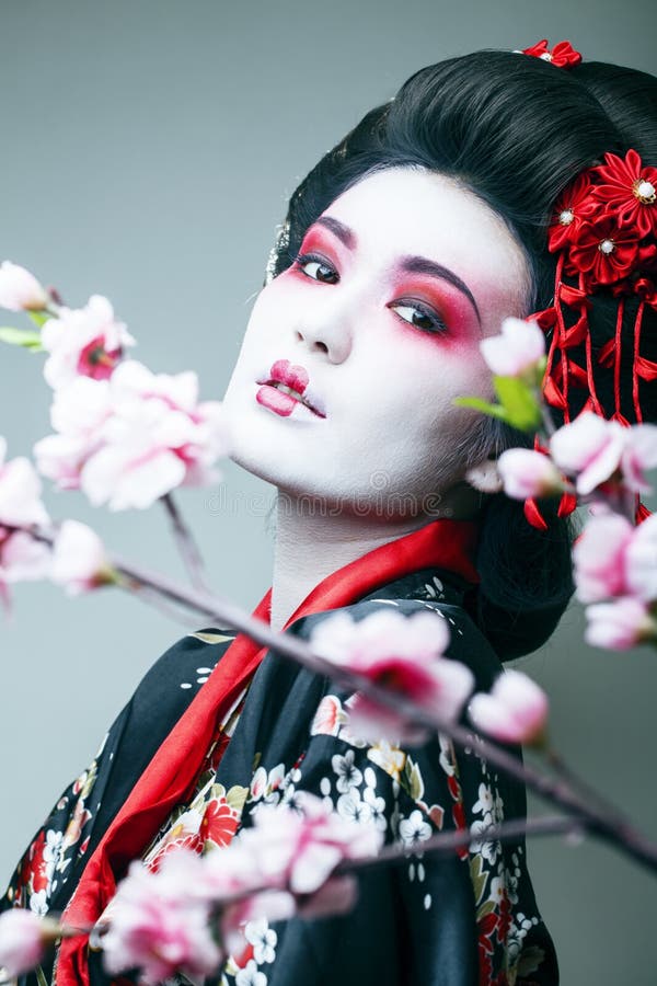 Jonge mooie geisha in zwarte kimono onder sakura, Aziatische ethnoclose-up stock afbeelding Jonge mooie geisha in zwarte kimono onder sakura, Aziatische ethnoclose-up stock afbeelding