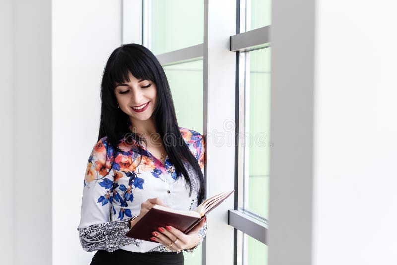 Jonge Mooie gelukkige vrouw die zich dichtbij het venster bevinden, schrijvend in notitieboekje, kijkend aan het notitieboekje, h stock foto's Jonge Mooie gelukkige vrouw die zich dichtbij het venster bevinden, schrijvend in notitieboekje, kijkend aan het notitieboekje, h stock foto's