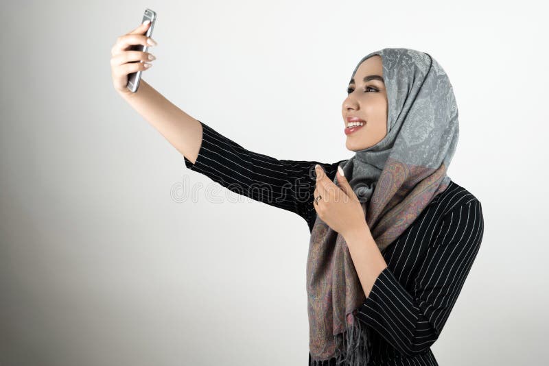 Jonge mooie glimlachende gelukkige Moslimvrouw in glazen die tulband dragen hijab, headscarf holdingssmartphone die a schieten stock fotografie Jonge mooie glimlachende gelukkige Moslimvrouw in glazen die tulband dragen hijab, headscarf holdingssmartphone die a schieten stock fotografie
