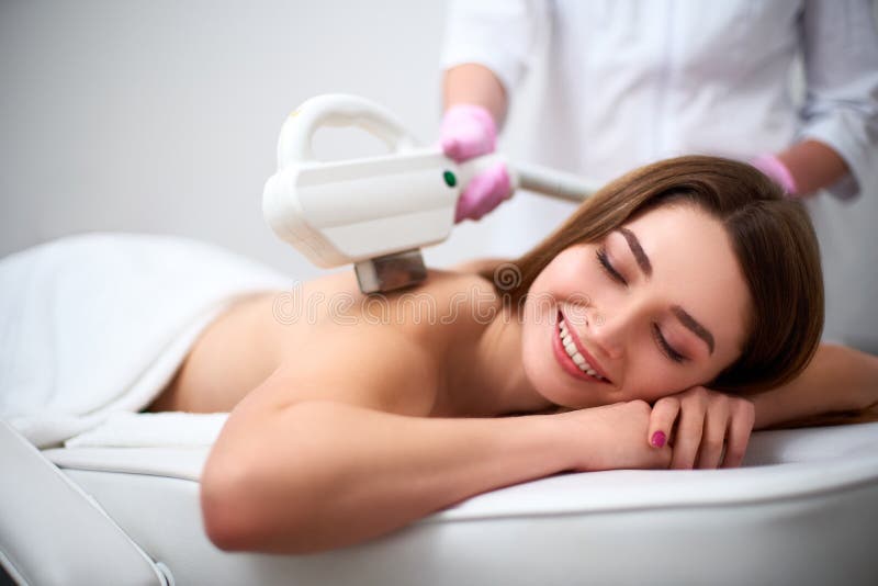 Jonge mooie het glimlachen epilation van de vrouwen achterlaser in schoonheidssalon Cosmetologist die ontharingsbehandeling met e royalty-vrije stock fotografie Jonge mooie het glimlachen epilation van de vrouwen achterlaser in schoonheidssalon Cosmetologist die ontharingsbehandeling met e royalty-vrije stock fotografie
