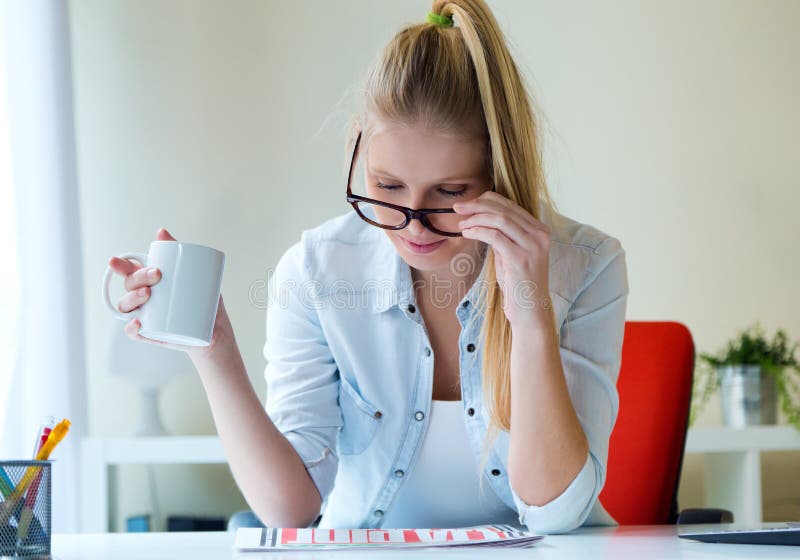 Jonge mooie vrouw die een kop van koffie houden en newspa lezen stock fotografie Jonge mooie vrouw die een kop van koffie houden en newspa lezen stock fotografie
