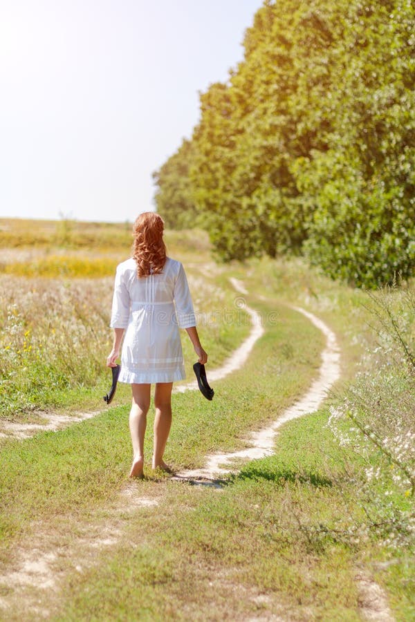 Jonge mooie vrouw die in gras lopen blootvoets en schoenen in handen houden stock afbeelding Jonge mooie vrouw die in gras lopen blootvoets en schoenen in handen houden stock afbeelding