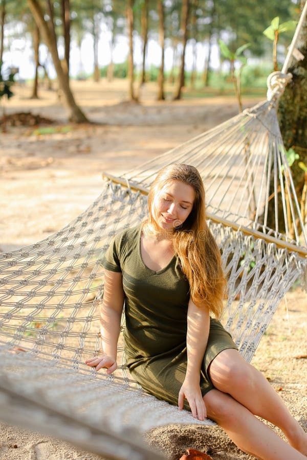 Jonge mooie vrouw die groene kledingszitting op rieten hangmat met zand en palmen op achtergrond dragen stock fotografie Jonge mooie vrouw die groene kledingszitting op rieten hangmat met zand en palmen op achtergrond dragen stock fotografie