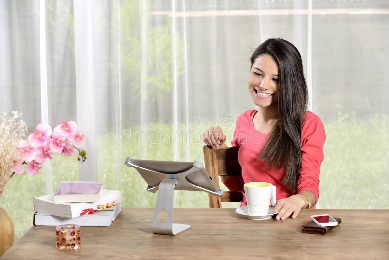 Young pretty woman holding cup of coffee and Ipad looking away. mobile phone on the table. Young pretty woman holding cup of coffee and Ipad looking away. mobile phone on the table