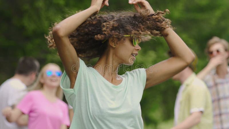 Jonge mooie vrouw met krullend haar die bij picknick met vrienden dansen, zomer