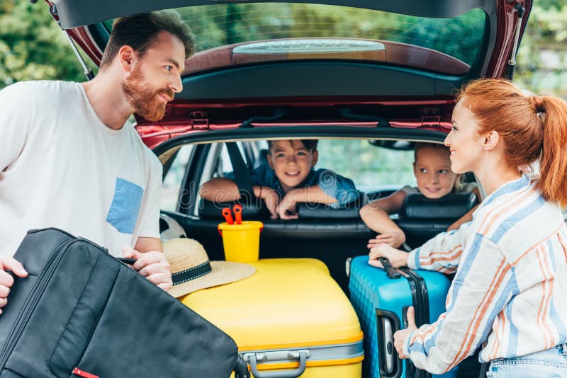 jonge ouders die bagage in boomstam van auto met jonge geitjes inpakken royalty-vrije stock fotografie jonge ouders die bagage in boomstam van auto met jonge geitjes inpakken royalty-vrije stock fotografie