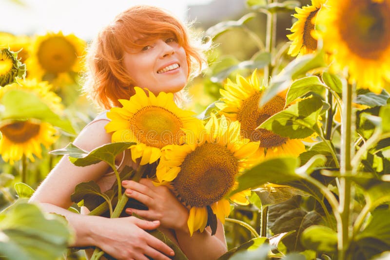 Jonge redheaded vrouw die op het gebied van zonnebloemen een reusachtige bos van bloemen in een zonnige de zomeravond houden royalty-vrije stock afbeeldingen Jonge redheaded vrouw die op het gebied van zonnebloemen een reusachtige bos van bloemen in een zonnige de zomeravond houden royalty-vrije stock afbeeldingen