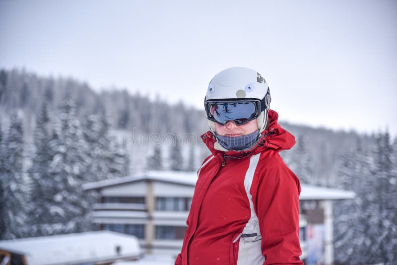Jonge ski?ende vrouw met zwarte beschermende brillen, witte helm en rood jasje, de wintertoevlucht op achtergrond stock foto Jonge ski?ende vrouw met zwarte beschermende brillen, witte helm en rood jasje, de wintertoevlucht op achtergrond stock foto